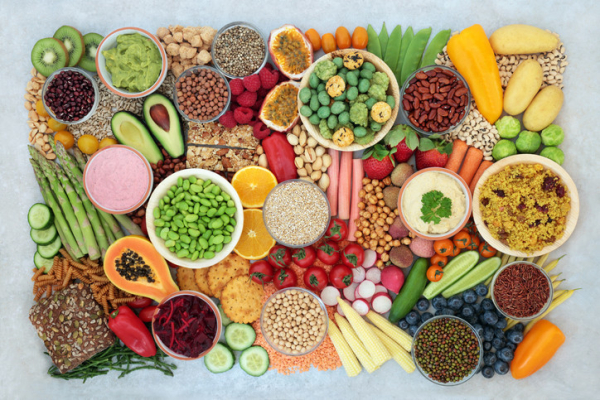 A brightly colored selection of plant-based vegan foods, including vegetables, fruit, grains, nuts, seeds, and vegan dips.